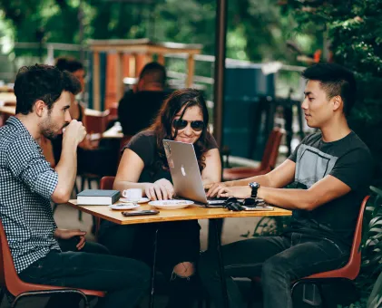 3 people sat in a cafe outside working on laptops